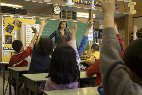 Image of students in a classroom with their hands raised.